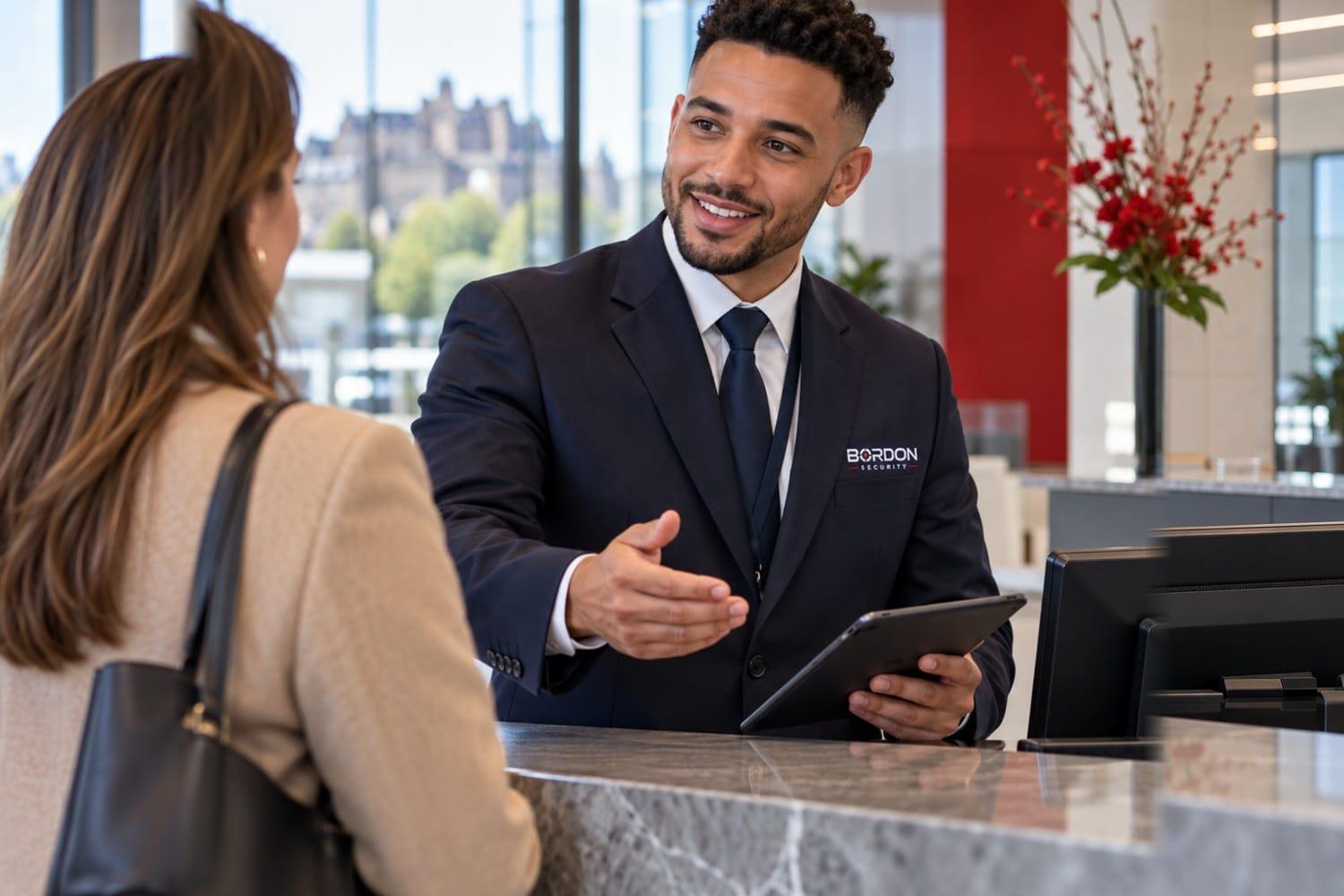 A Bordon Security officer at a reception desk welcomes a visitor with an open hand, holding a tablet, in a bright office lobby.